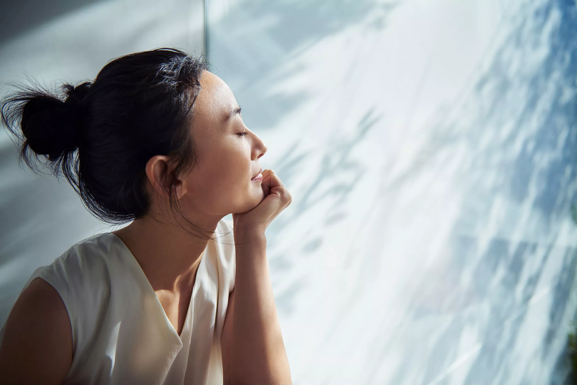 A person sits peacefully with eyes closed, in soft natural light, with leafy shadows in the background.