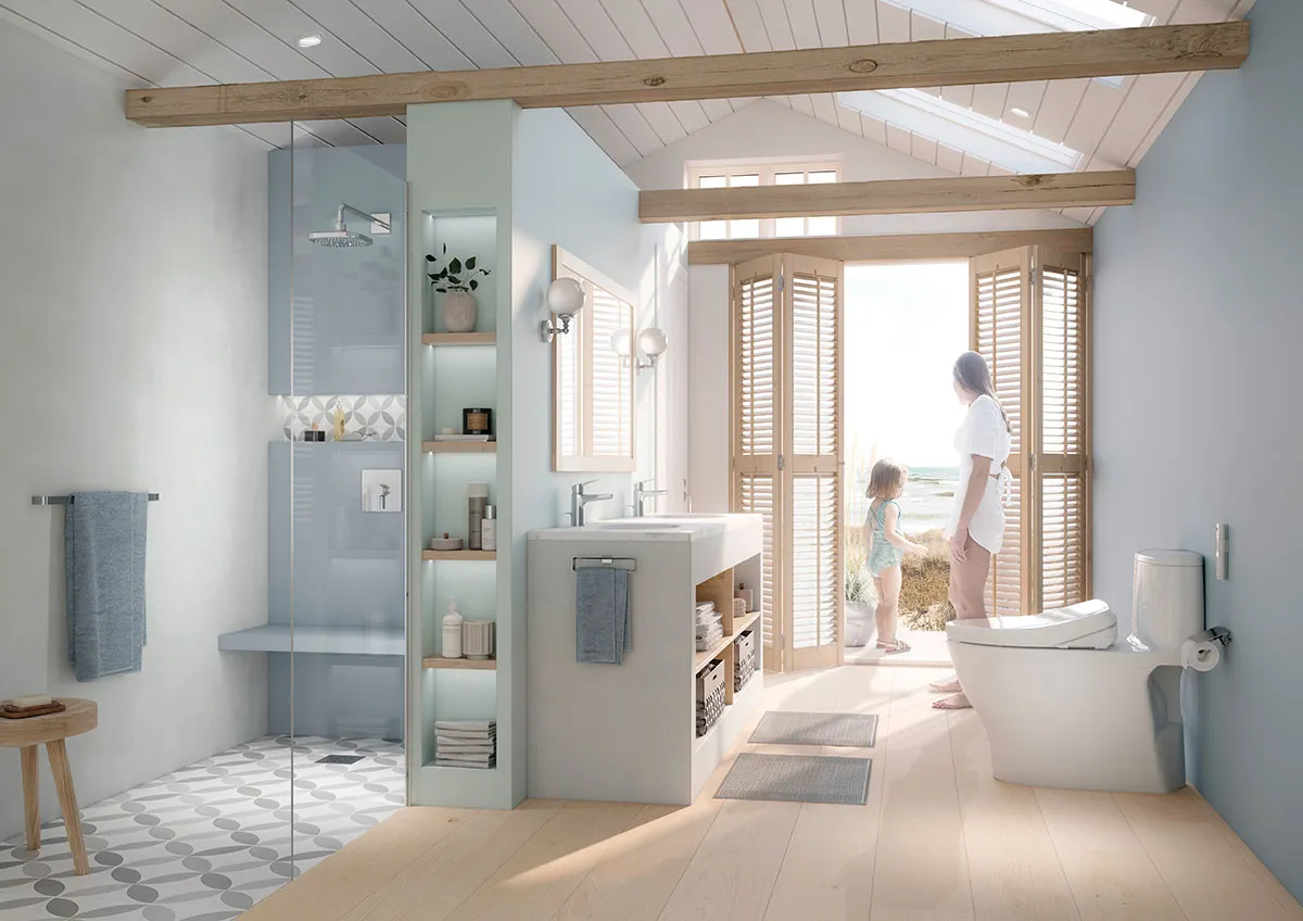 A mother and child stand at open doors overlooking the beach in a bright bathroom featuring a Nexus WASHLET plus bidet toilet near the vanity.