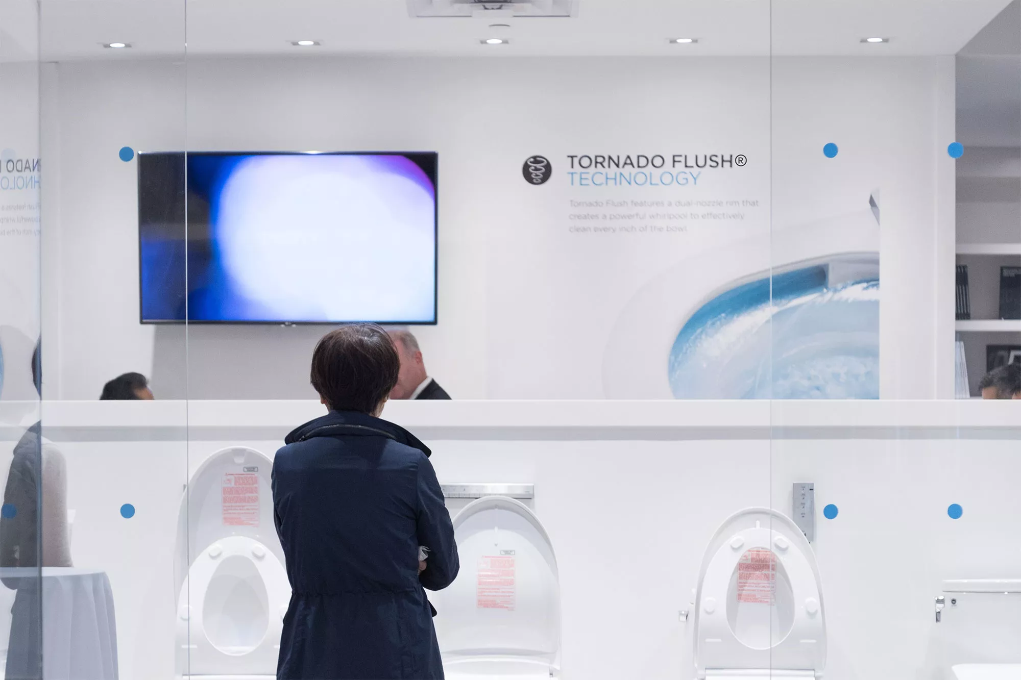 A person observing a row of TOTO toilets beneath a display highlighting Tornado Flush technology.