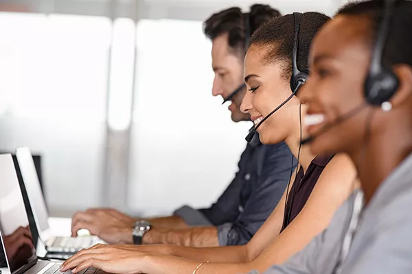 Smiling customer service employees with headsets at laptops