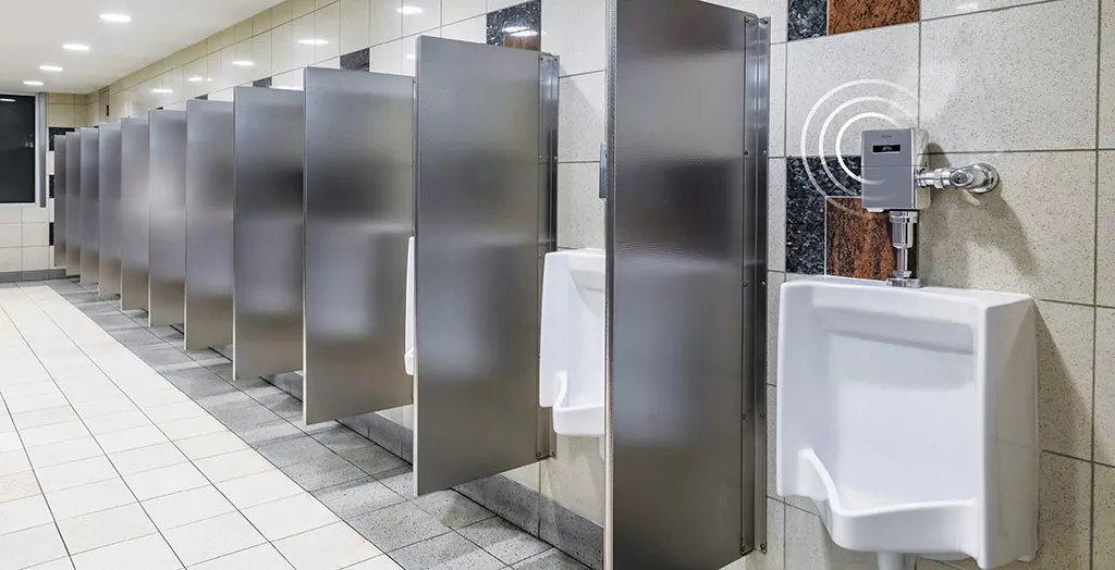 A commercial restroom with TOTO IoT-enabled urinal flush valves, stainless steel partitions, and tiled walls and flooring.