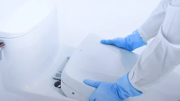 Person wearing gloves gently removing a WASHLET bidet seat from a toilet, demonstrating the correct removal technique