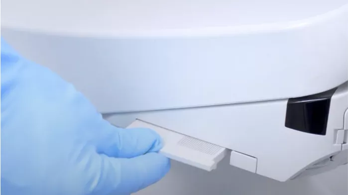 Gloved hand pulling out the deodorizer filter from a WASHLET bidet seat, demonstrating routine maintenance care